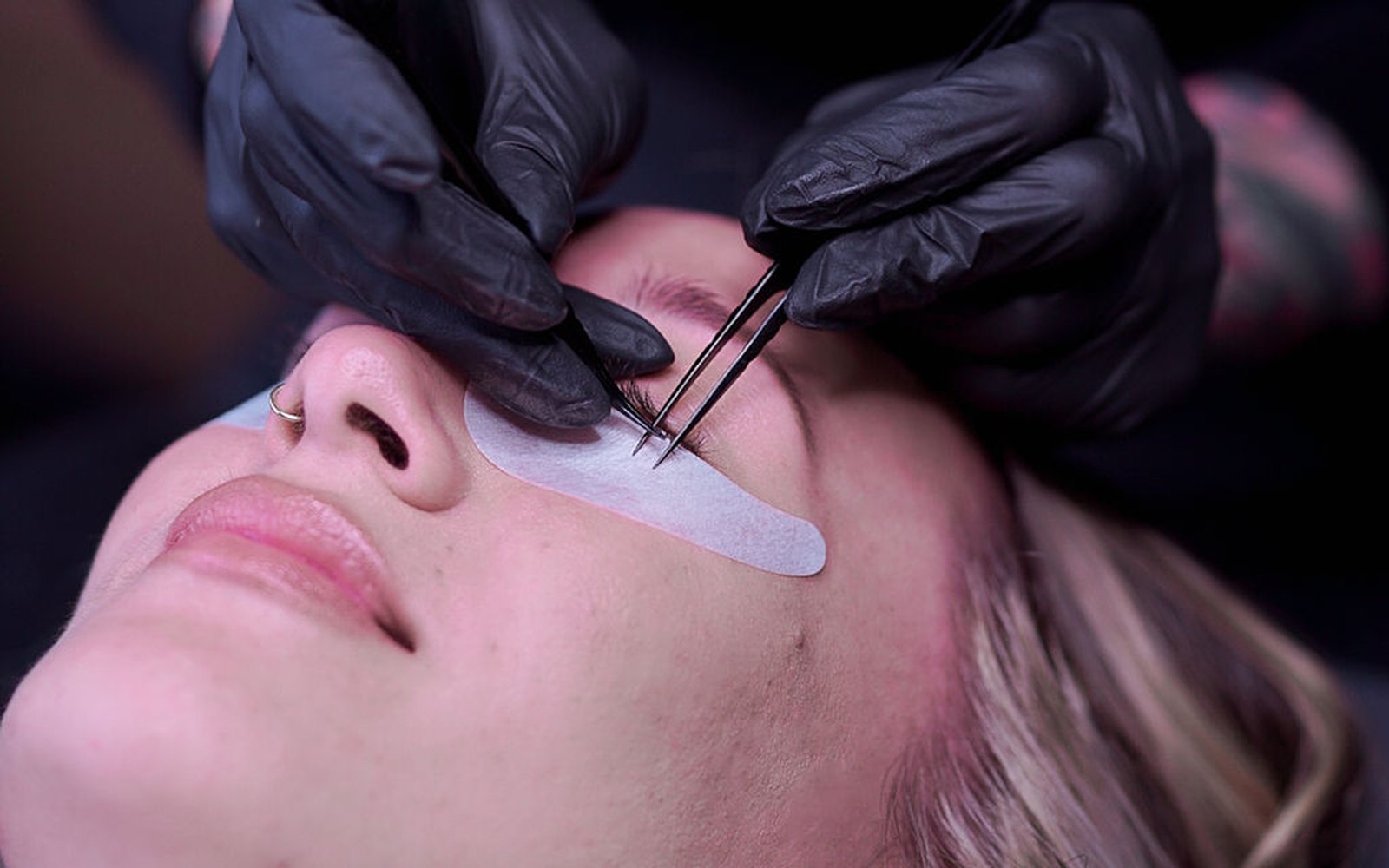 Lash artist working on a client's lashes with two tweezers