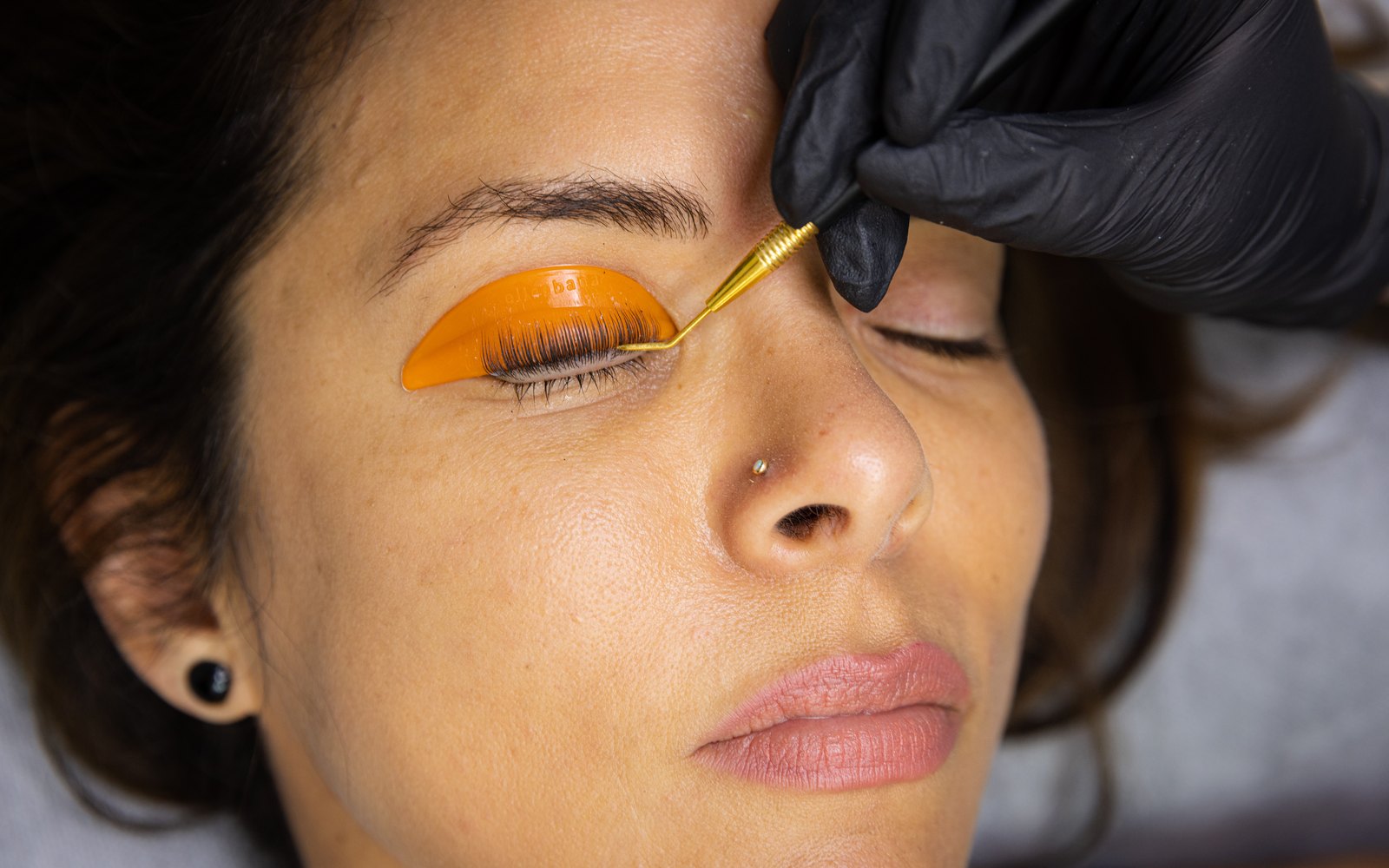 Gold lifting tool sweeping lashes onto an orange silicone shield